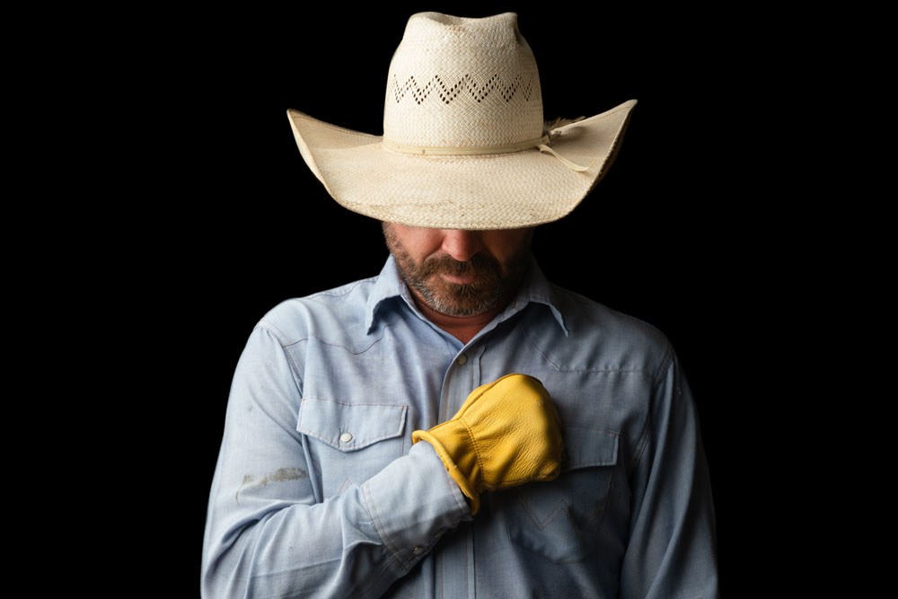 Rancher with cowboy hat, holding yellow-gloved hand over his heart.
