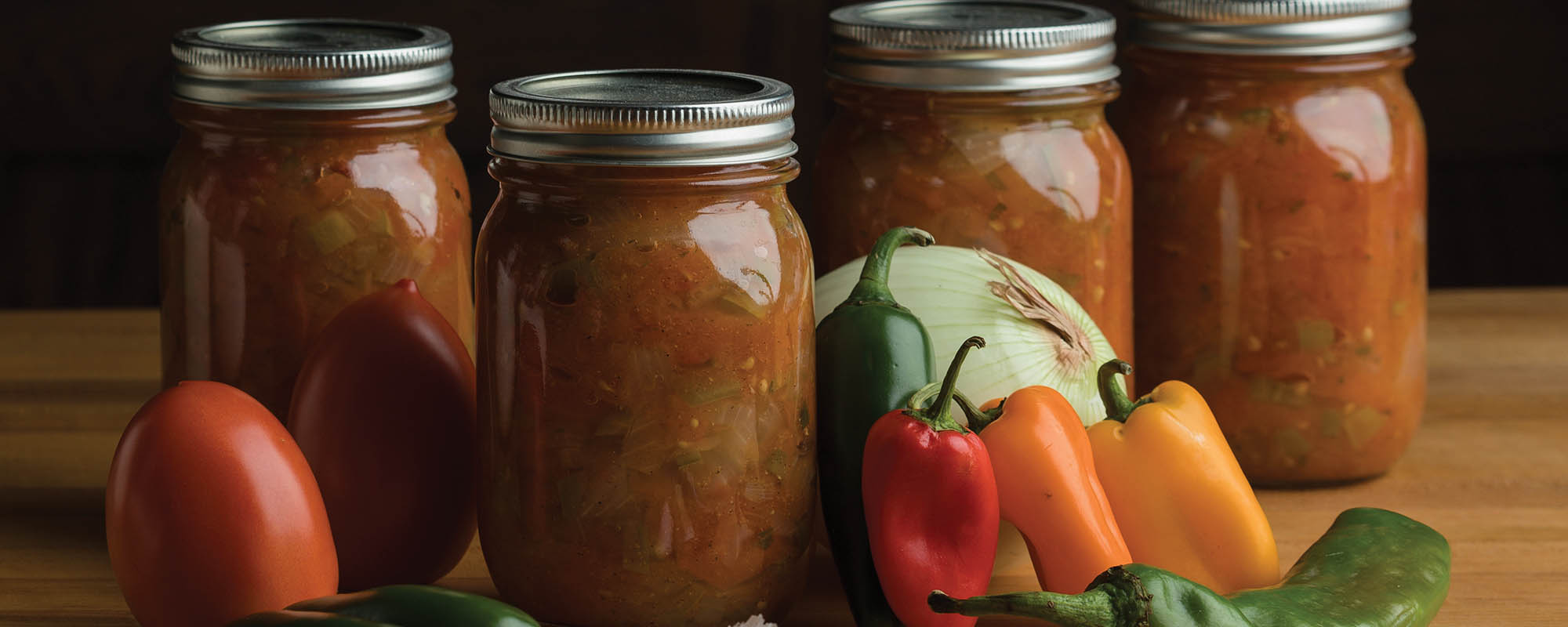 Jars of salsa with vegetables around them