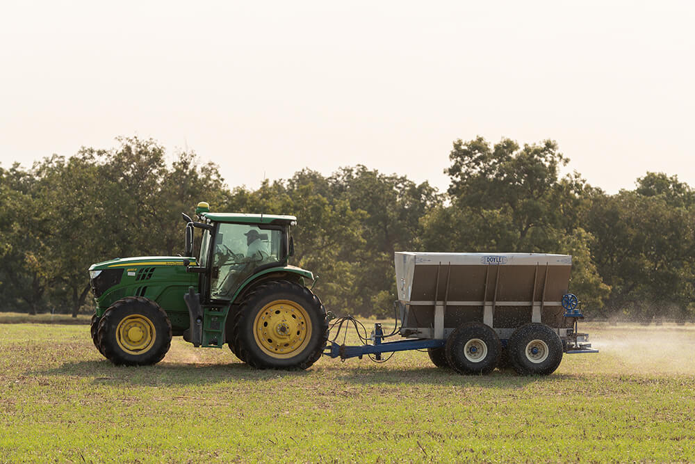 Tractor speading solid nitrogen fertilizer at Red River Ranch